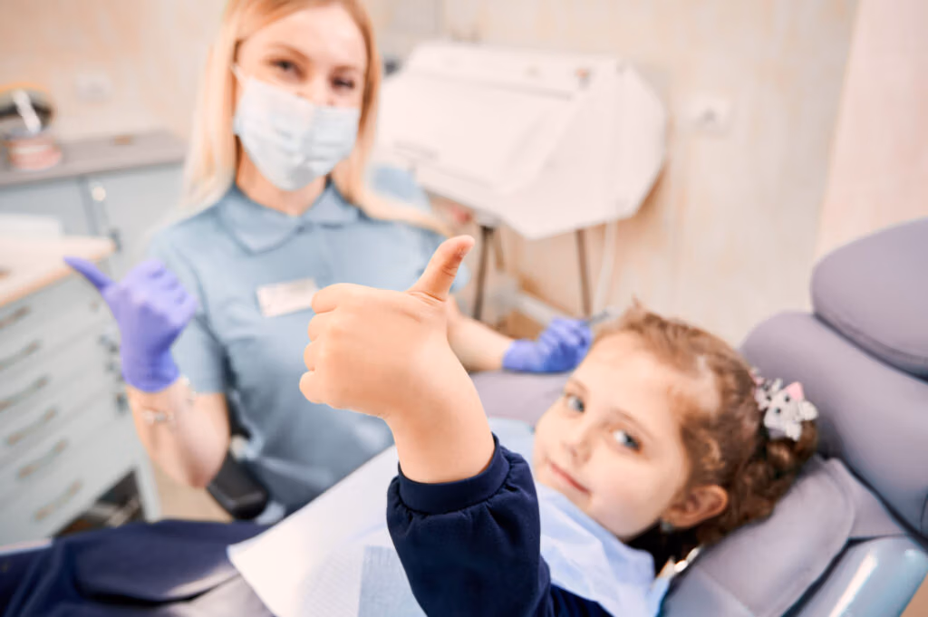 Female dentist and a smiling little girl giving thumbs up